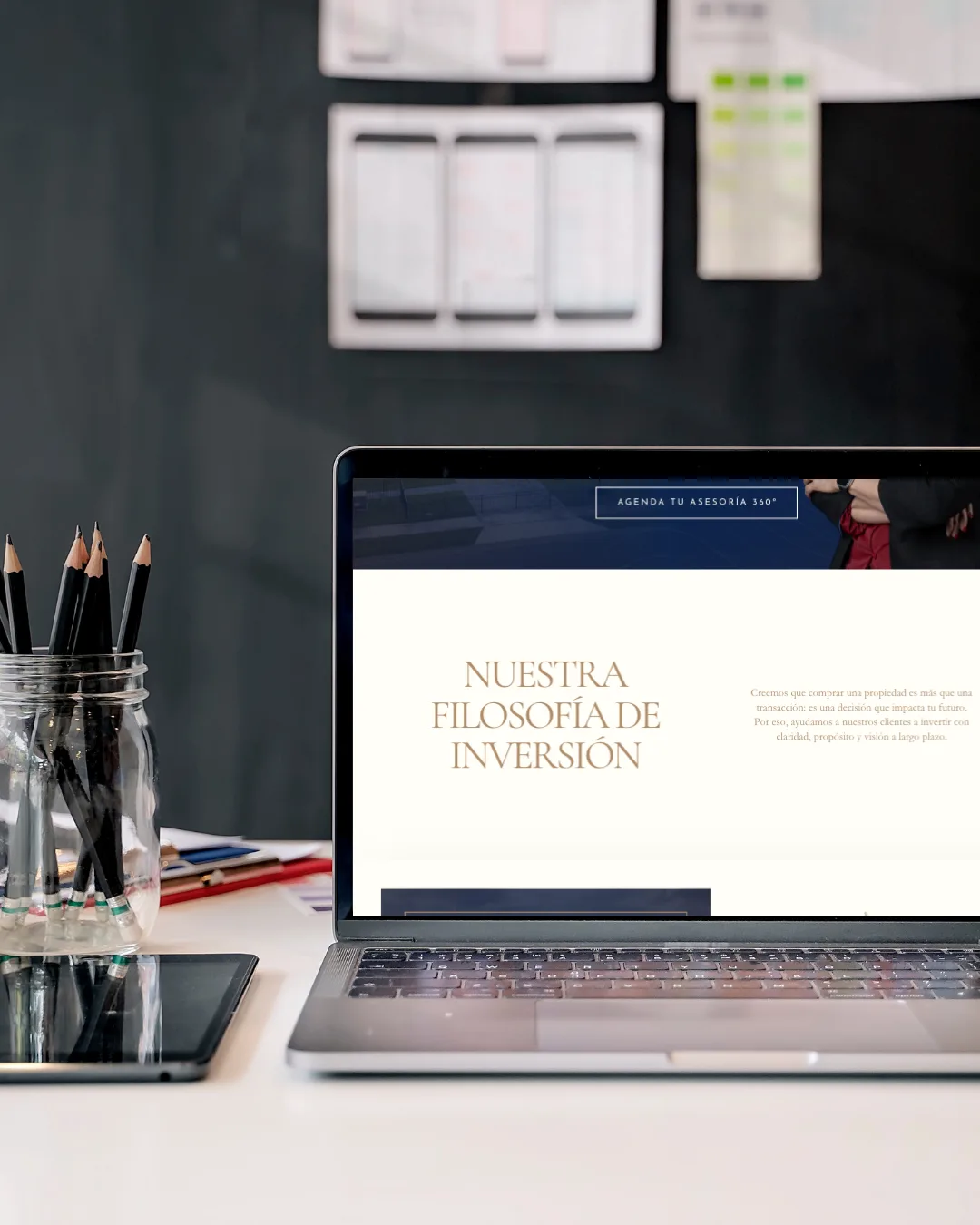 The new site on a laptop: "Nuestra filosofía de inversión" set in serif capitals on a cream editorial page.